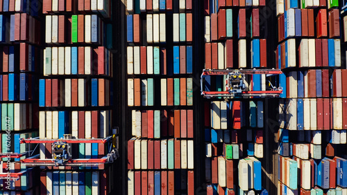 Rows of cargo containers rest atop massive container ships docked at an industrial port. Aerial view cargo ship terminal. Aerial view of shipping container port terminal. 