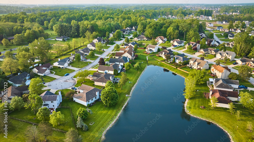 Dark blue pond with housing neighborhood and cul-de-sac suburban homes in summer aerial