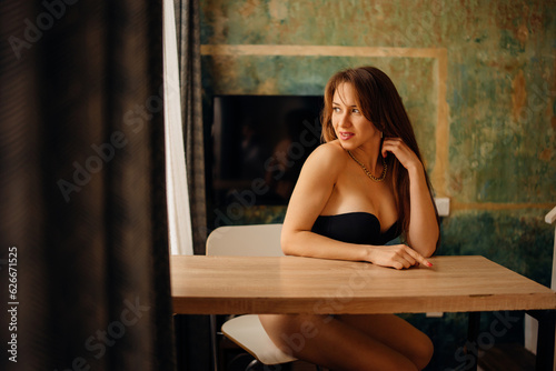 Portrait of a beautiful and sexy young woman in a black bustier at a table.  photo