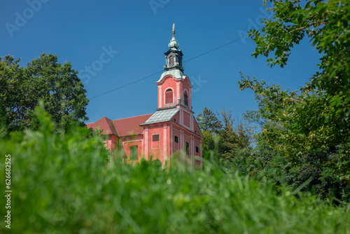 Red church on Rozik hill above Ljubljana surrounded by lush green trees and grassy meadows. Beautiful scenery around a tyoical church.