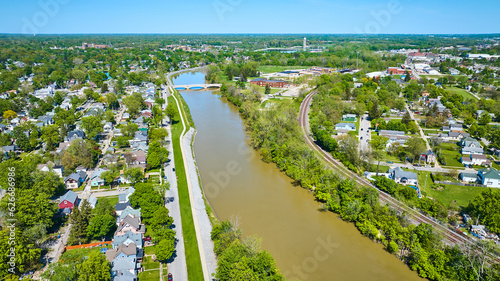 Suburban houses next to large muddy river and winding train tracks aerial city © Nicholas J. Klein