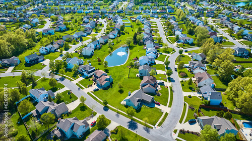Фотография Aerial large suburbs of multiple colored houses with nearby pond with water foun