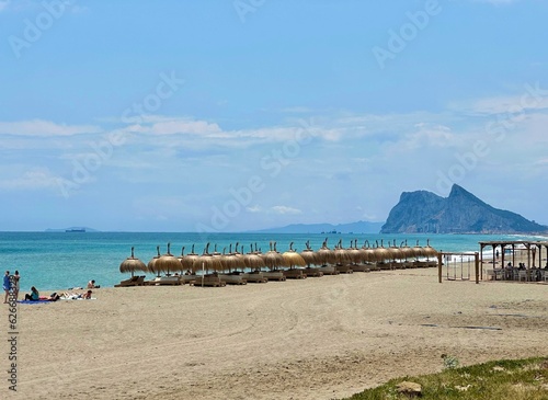 Umbrellas and sunbeds on a sandy beach in La Alcaidesa with the Rock of Gibraltar in the background, vacation, recreation, tourism, Playa de la Hacienda, Mediterranean Sea, Andalusia, Malaga, Spain photo