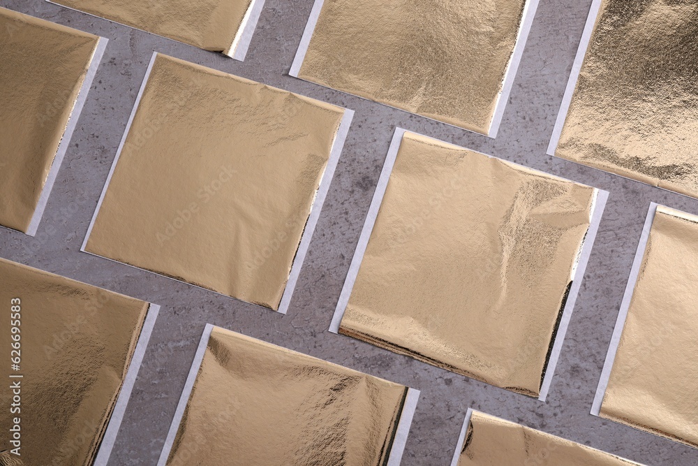 Fototapeta premium Many edible gold leaf sheets on grey textured table, flat lay