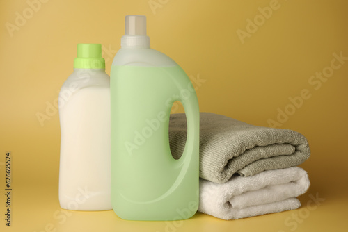 Bottles of fabric softener and stacked clean towels on pale yellow background