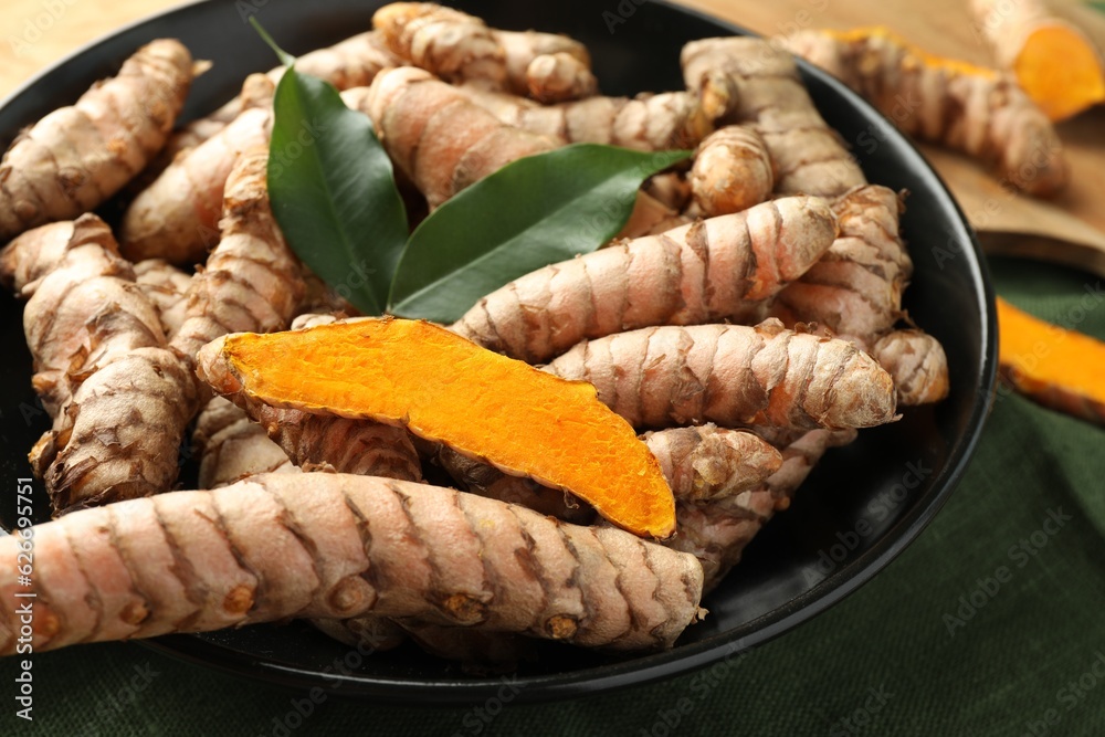 Bowl with raw turmeric roots and green leaves on table, closeup Bowl with raw turmeric roots and green leaves on table, closeup