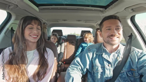 Front view of happy loving parents and their excited kids smiling driving car in the city. Young family traveling abroad by car in summer. Concept of happy childhood. Family trip. Auto tourism.