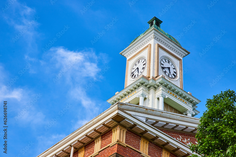 Clock tower on brick building roof with blue skies and green tree top Clock tower on brick building roof with blue skies and green tree top
