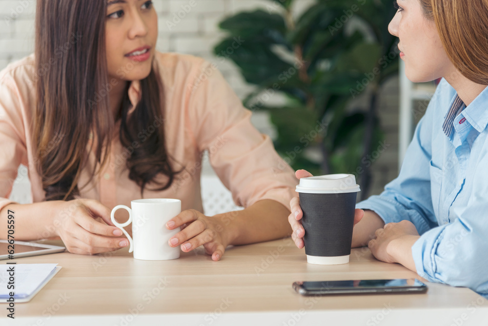 Two Women colleagues drinking black coffee cup at office desk together. Asian woman friendstalking smiling with friendship happy time. Teamwork happy moment lifestyle. International Woman day concept Two Women colleagues drinking black coffee cup at office desk together. Asian woman friendstalking smiling with friendship happy time. Teamwork happy moment lifestyle. International Woman day concept