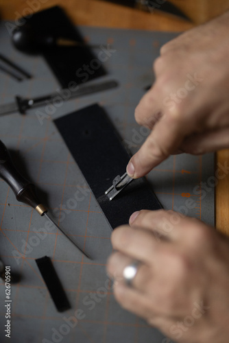 Man doing leatherwork, in a leather working workshop, making a black leather belt