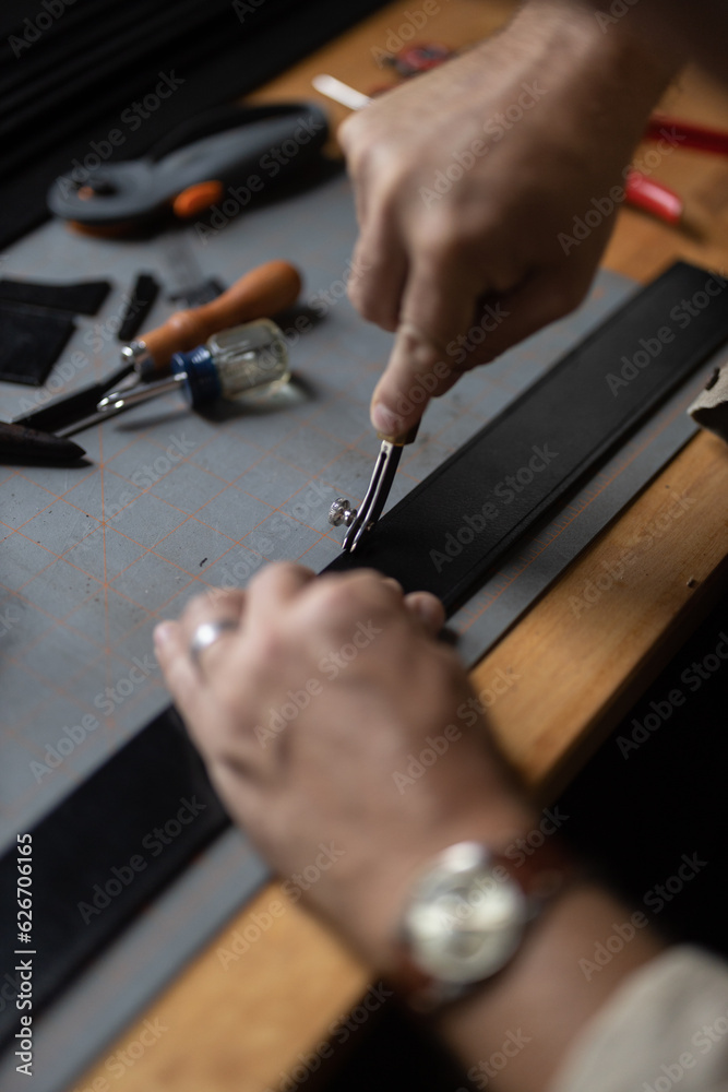 Man doing leatherwork, in a leather working workshop, making a black leather belt Man doing leatherwork, in a leather working workshop, making a black leather belt