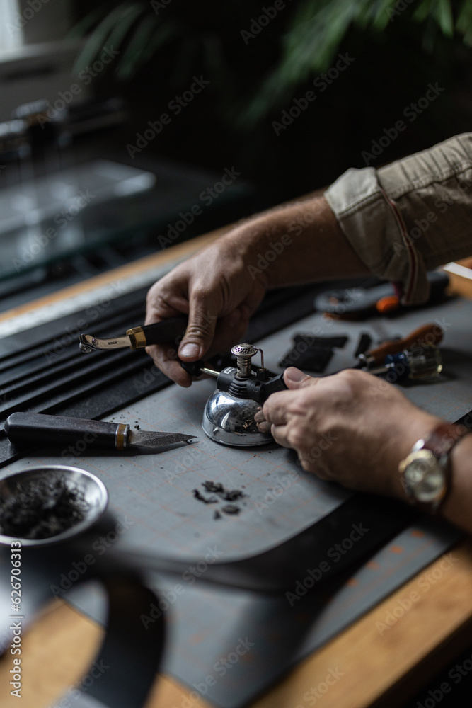 Man doing leatherwork, in a leather working workshop, making a black leather belt Man doing leatherwork, in a leather working workshop, making a black leather belt