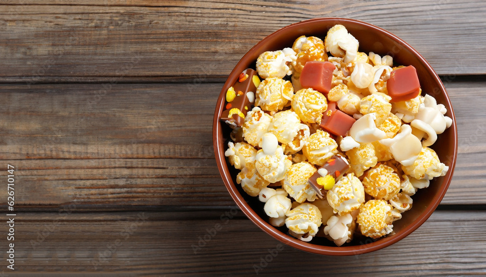 Delicious popcorn with caramel in bowl and candies on wooden background, top view Delicious popcorn with caramel in bowl and candies on wooden background, top view