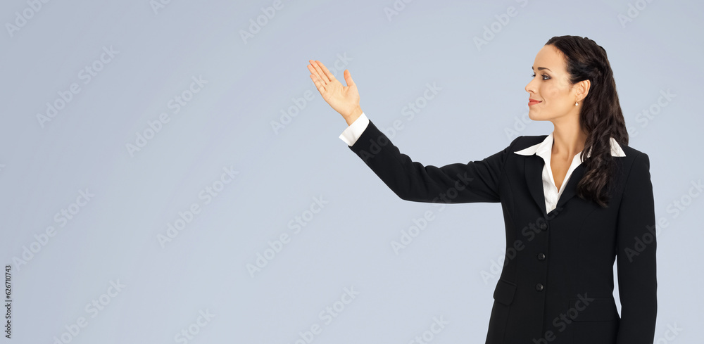 Image of smiling woman in black confident suit, showing at copy space. Business concept. Isolated over grey background. Brunette businesswoman. Image of smiling woman in black confident suit, showing at copy space. Business concept. Isolated over grey background. Brunette businesswoman.