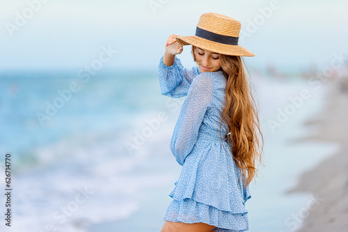 Obraz na płótnie Beautiful teenager girl on tropical seashore at sunset. Beautiful little girl in dress at beach having fun. Happy girl enjoy summer vacation background the blue sky and turquoise water in the sea w salonie