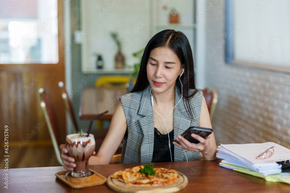 Asian beautiful woman sitting in a small restaurant Preparing to eat lunch alone Order pizza and coffee to eat. along with listening to music via smartphones for enjoyment
