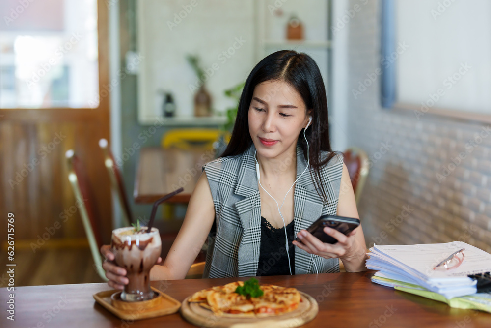 Asian beautiful woman sitting in a small restaurant Preparing to eat lunch alone Order pizza and coffee to eat. along with listening to music via smartphones for enjoyment Asian beautiful woman sitting in a small restaurant Preparing to eat lunch alone Order pizza and coffee to eat. along with listening to music via smartphones for enjoyment