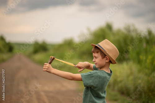 child boy of primary school age holds a slingshot in his hands plays and squinted his eye photo
