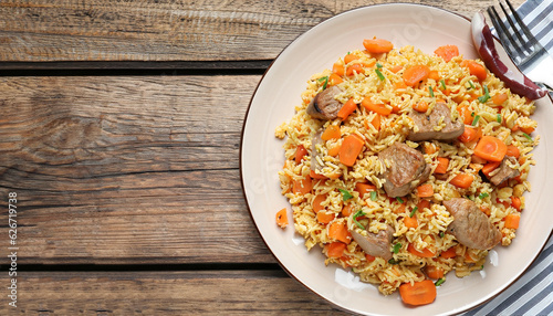 Delicious pilaf with meat, carrot and garlic on wooden table, top view. Space for text