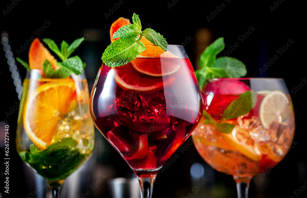 Red, white, rose sangria summer alcoholic cocktail drinks with spanish wine, fruits, citrus and ice. Black bar counter background, steel bar tools and bottles