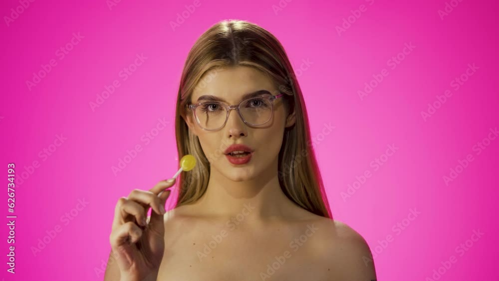 Attractive caucasian woman looking at camera and licks a yellow lollipop, studio