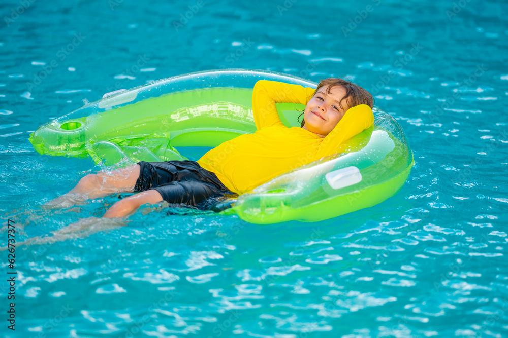 Happy child enjoying summer vacation outdoors in water in the swimming pool. Cute little kid in swimming suit relaxing on an inflatable ring. Kid floating in a pool.