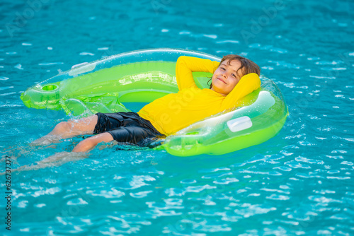 Happy child enjoying summer vacation outdoors in water in the swimming pool. Cute little kid in swimming suit relaxing on an inflatable ring. Kid floating in a pool.