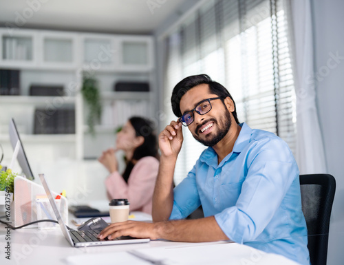 Indian professional business man, businessman wearing glasses working on computer, looks directly at camera and smiles friendly