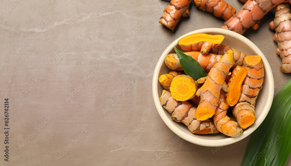 Bowl with raw turmeric roots and green leaves on light brown table, flat lay. Space for text Bowl with raw turmeric roots and green leaves on light brown table, flat lay. Space for text