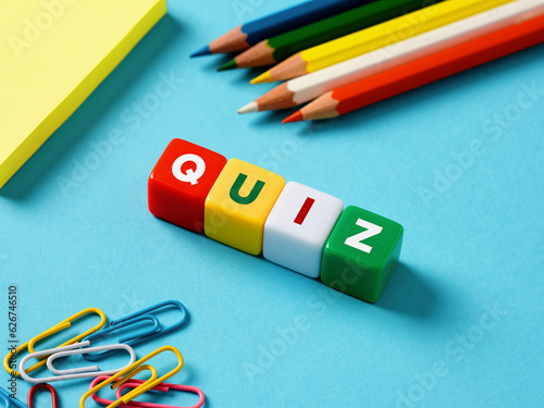 Educational exam or question games concept. The word quiz on colorful cubes with stationery objects on blue background.