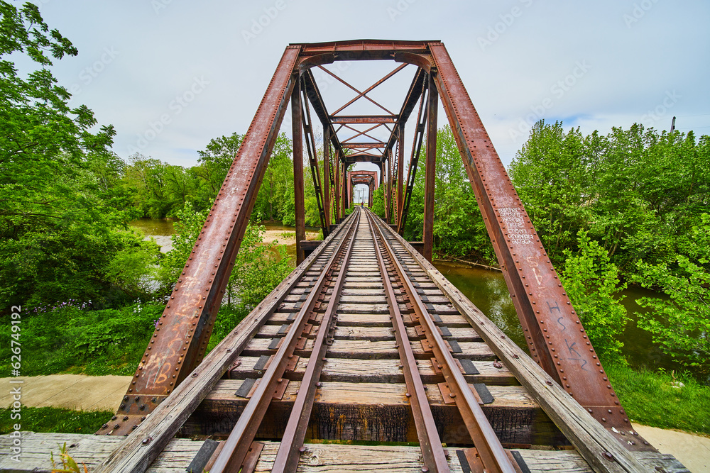 Train tracks on iron truss railroad bridge over Kokosing River with distant person walking Train tracks on iron truss railroad bridge over Kokosing River with distant person walking