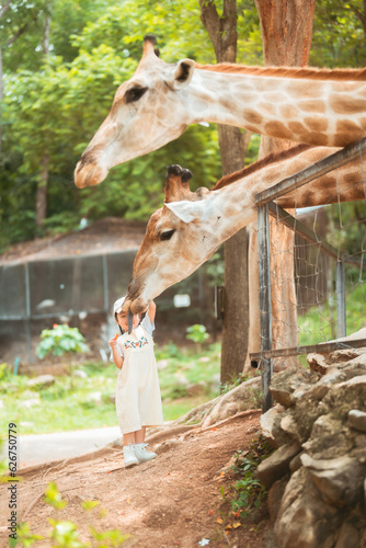 cute baby girl in dress and hat with activity feed food giraffe with happy time on outdoor