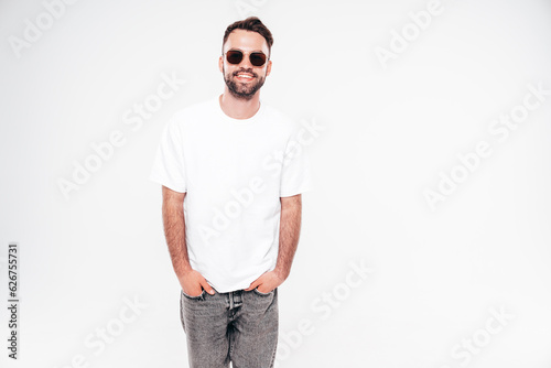 Portrait of handsome smiling stylish hipster lambersexual model. Sexy man dressed in white T-shirt and jeans. Fashion male isolated on white background in studio. In sunglasses