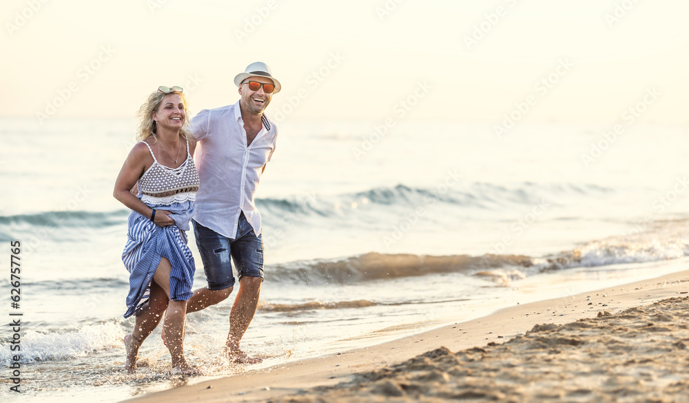 Happy middle-aged couple in love walking in the water on the beach at sunset. Happy middle-aged couple in love walking in the water on the beach at sunset.