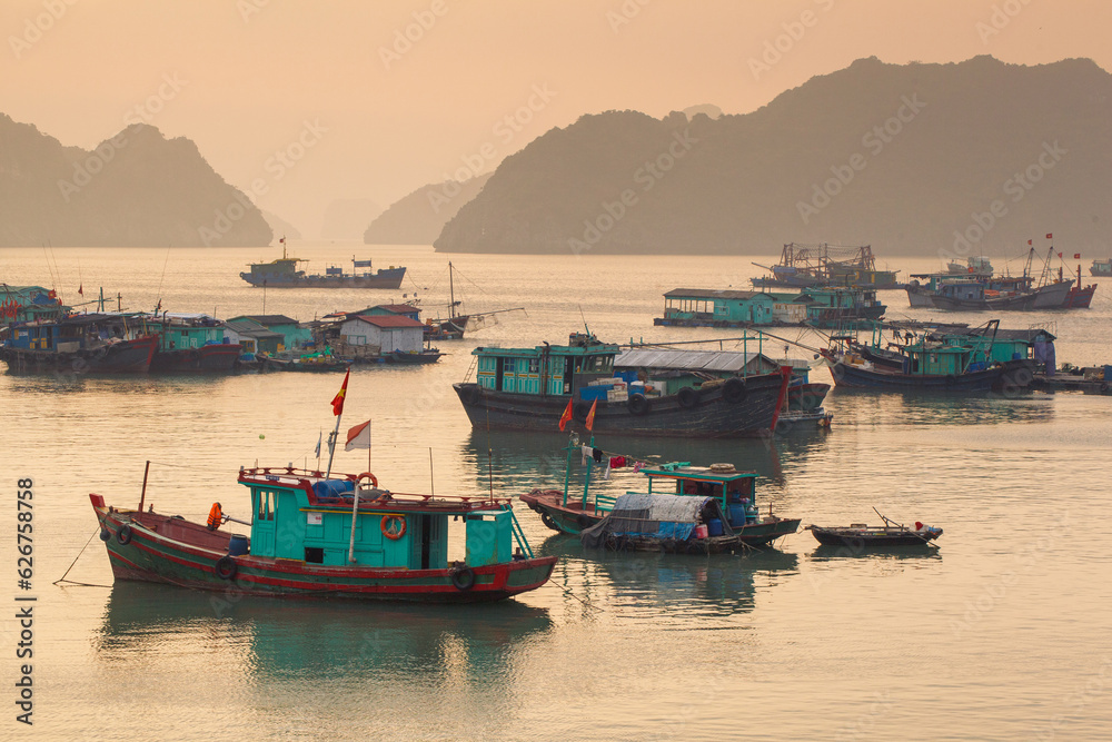 Fototapeta premium Colorful fishing boats on a sea near to rock islands on sunset. Ha Long Bay, Vietnam.