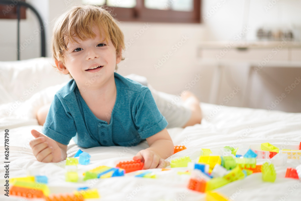 Happiness child playing developing colorful blocks. Smiling Kids play alone with a toy on bed at home. Kindergarten education game. Learn and Play Concept. Happiness child playing developing colorful blocks. Smiling Kids play alone with a toy on bed at home. Kindergarten education game. Learn and Play Concept.