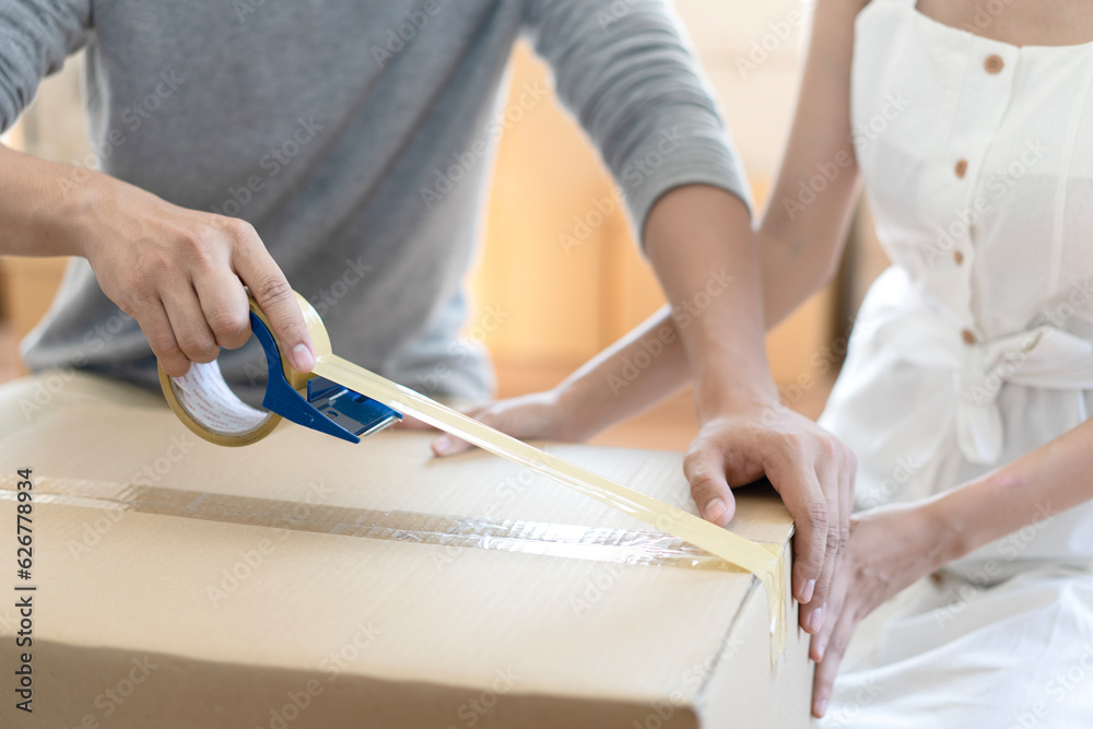 Couple of young asian helping pack machine, sealing cardboard boxes and delivery to customer at home. Startup small business entrepreneur or freelance Couple asian, Shipping delivery and SME concept.