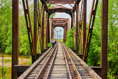 Valokuva Two people walking along train tracks on old iron railroad bridge over Kokosing