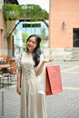 A beautiful Asian woman walks with her shopping bags and enjoys shopping at a city square