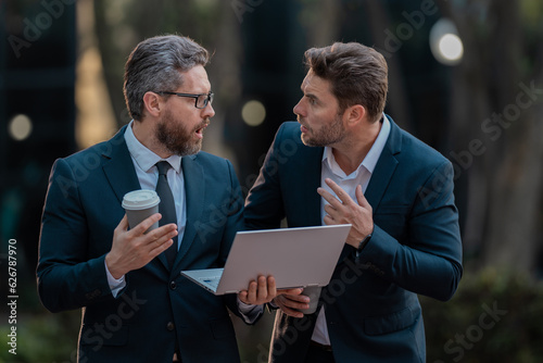 Excited suprised two business teams men team using tablet laptop outdoor. Business men team working on laptop outdoor. Businessmen looking laptop with their business success in city. Business success.