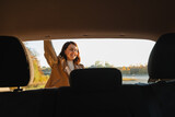 A smiling woman closes the trunk of the car, as seen from the inside of the vehicle