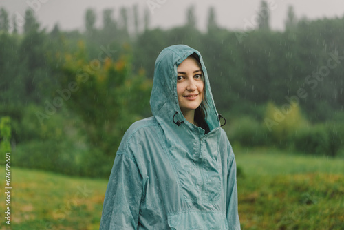 Portrait of a young girl in a blue raincoat enjoying the rain on a summer day.