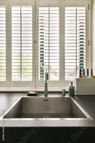 a kitchen sink and window with plantation shutters in the window behind it, which is open to let light into the room