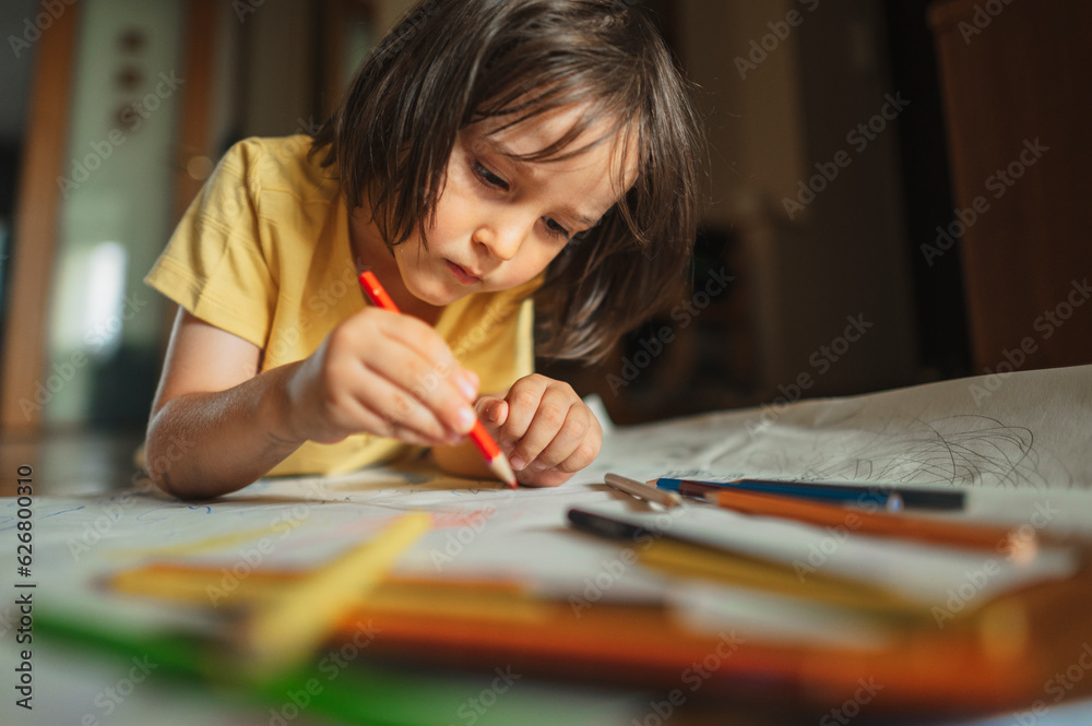 Focused boy drawing with colored pencil at home