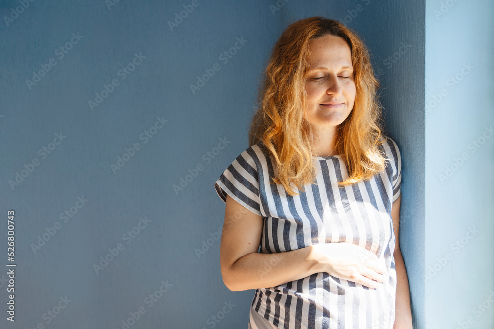 Pregnant woman with eyes closed touching stomach at home Pregnant woman with eyes closed touching stomach at home