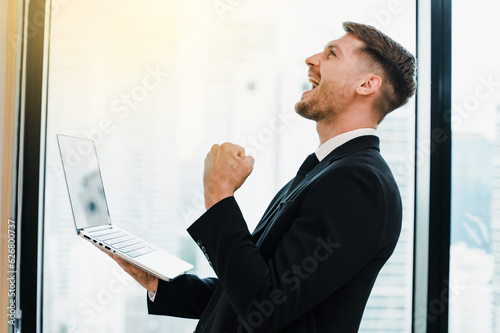 Portrait of happy business man celebrating victory success reading good news,with a laptop at the desk,received great results, got promoted.