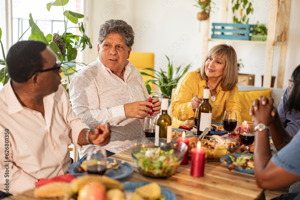 Multi-cultural senior friends talking to each other sitting at dining table Multi-cultural senior friends talking to each other sitting at dining table
