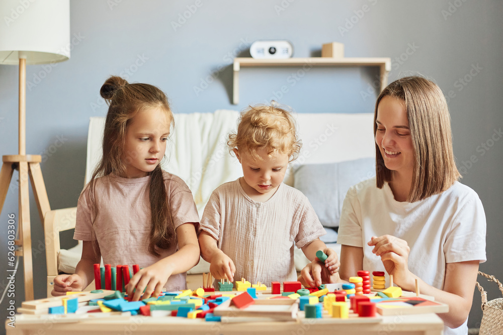 Fototapeta premium Happy childhood memories. Imaginative play sessions. Educational toy collection. Parental teaching moments. Charming children playing together with mother with wooden sorter toys at home interior.