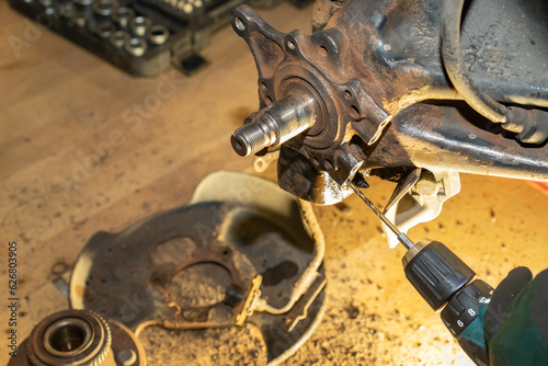 The car mechanic drills a thread. Repair wheel hub bearing. Workshop. Yellow light.