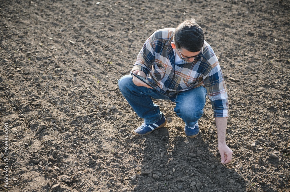 Farmer works in field in spring with tablet. An elderly farmer looks at tablet and green shoots. A smart, agronomist with tablet in his hands, checks field. Environmentally friendly farming. Farmer works in field in spring with tablet. An elderly farmer looks at tablet and green shoots. A smart, agronomist with tablet in his hands, checks field. Environmentally friendly farming.